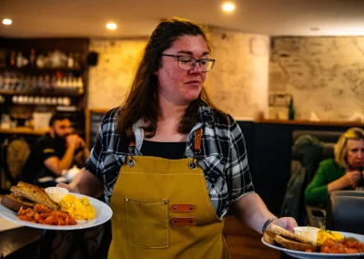 A staff member carrying a stack of breakfast plates through the dining room.