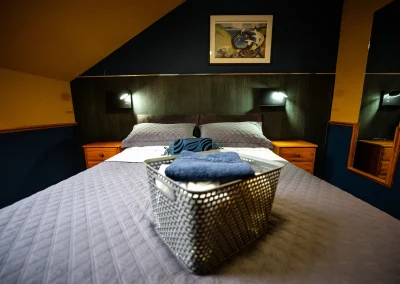 A hotel bedroom with a bed dressed in a grey quilted spread against a dark accent wall.