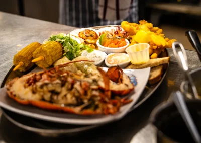 A large seafood sharing platter with grilled king scallops, calamari, smoked salmon, battered fish, corn on the cob, salad, lobster tail, bread and dips.