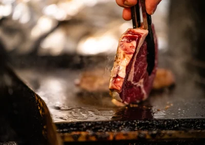 A raw steak held with tongs over a smoking hot chargrill.