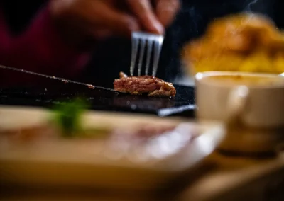 A piece of steak lifted with a fork from a sizzling hot stone.