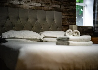 Made-up double bed with grey buttoned headboard and folded towels at Thorshaven Apartment